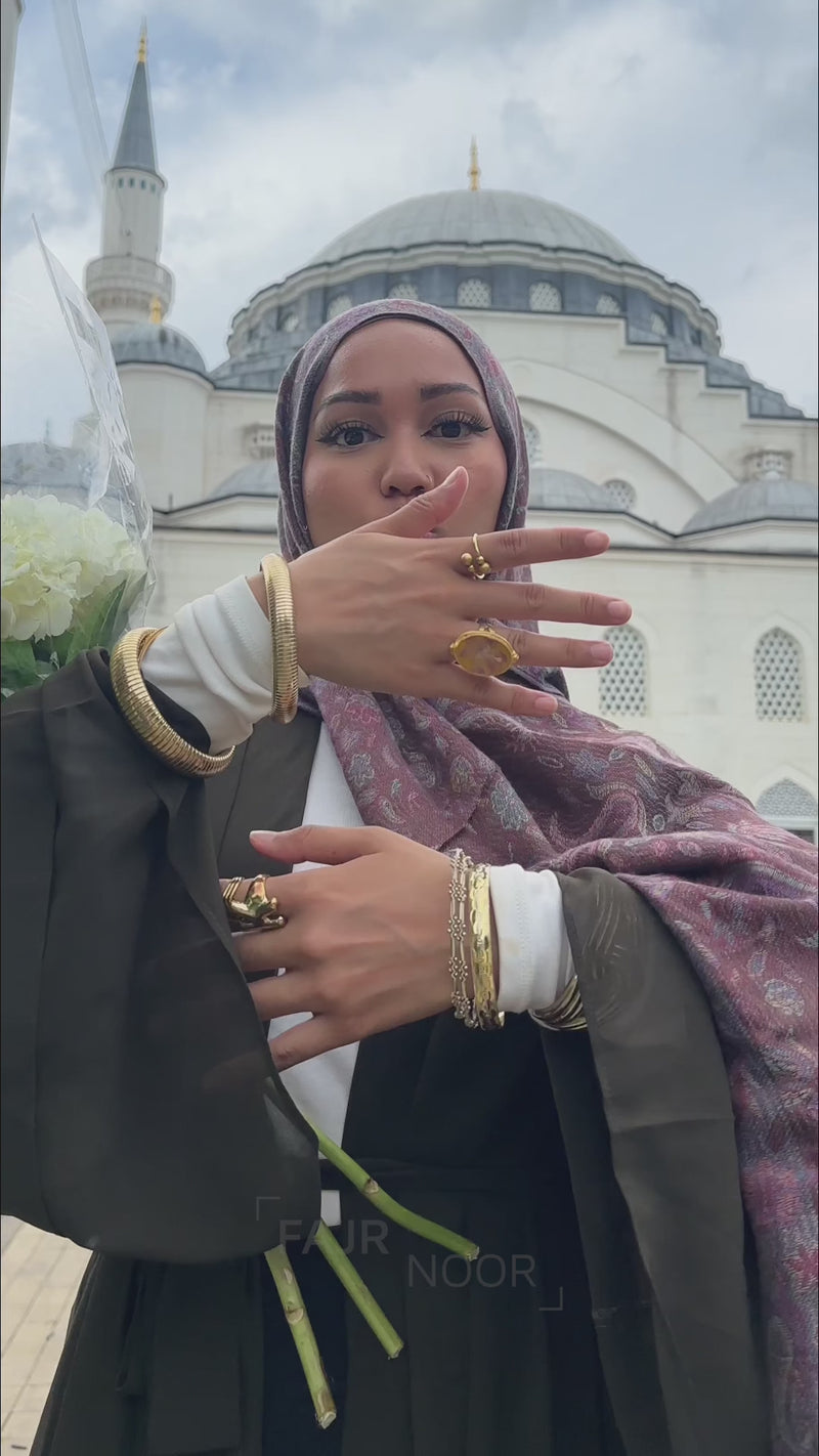 Woman wearing the Fajr Noor Aisha Abaya in khaki with a mauve patterned hijab, standing in front of a mosque