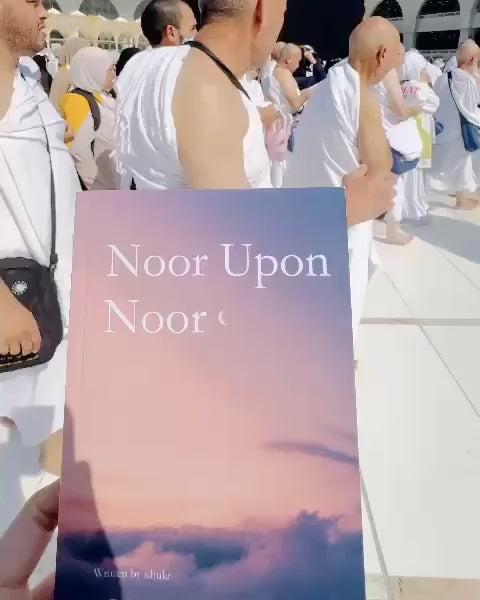 Fajr Noor "Noor Upon Noor" book held up in Mecca with pilgrims in the background