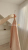 Fajr Noor Crinkle Abaya in cream held on a hanger by a window, showing the flowing crinkle texture
