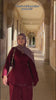 Woman wearing the Fajr Noor Sarah Set in maroon with a matching mauve pashmina hijab, walking through an elegant arched colonnade in a modest hijabi outfit.